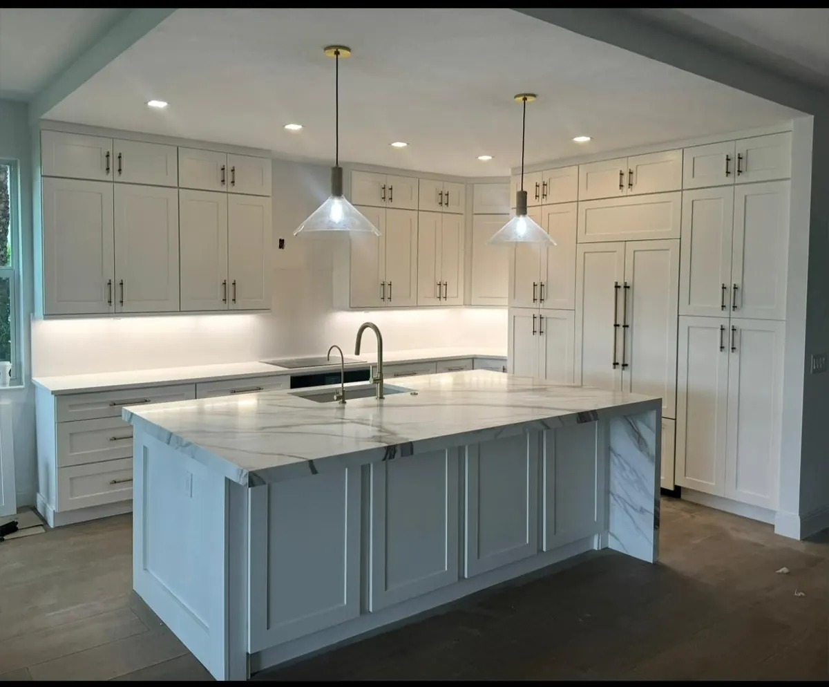 Remodeled white kitchen with a large marble-look island under glass pendant lights