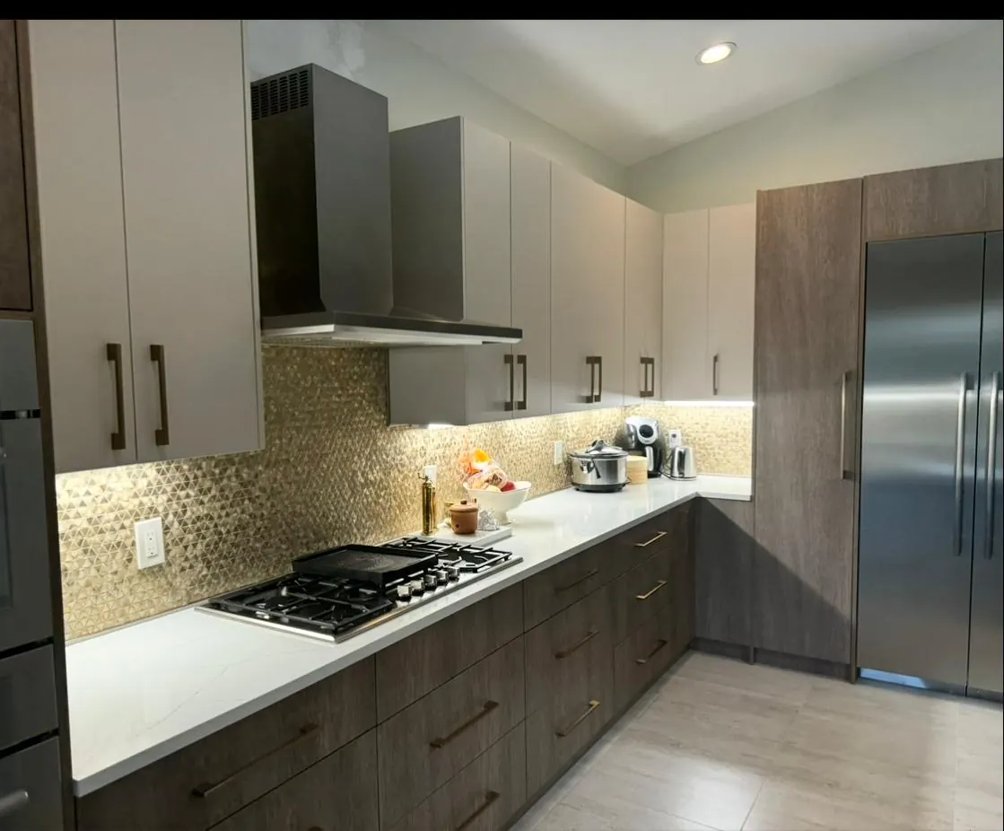 Gold mosaic backsplash, stainless range hood, and gas cooktop over wood-grain cabinets