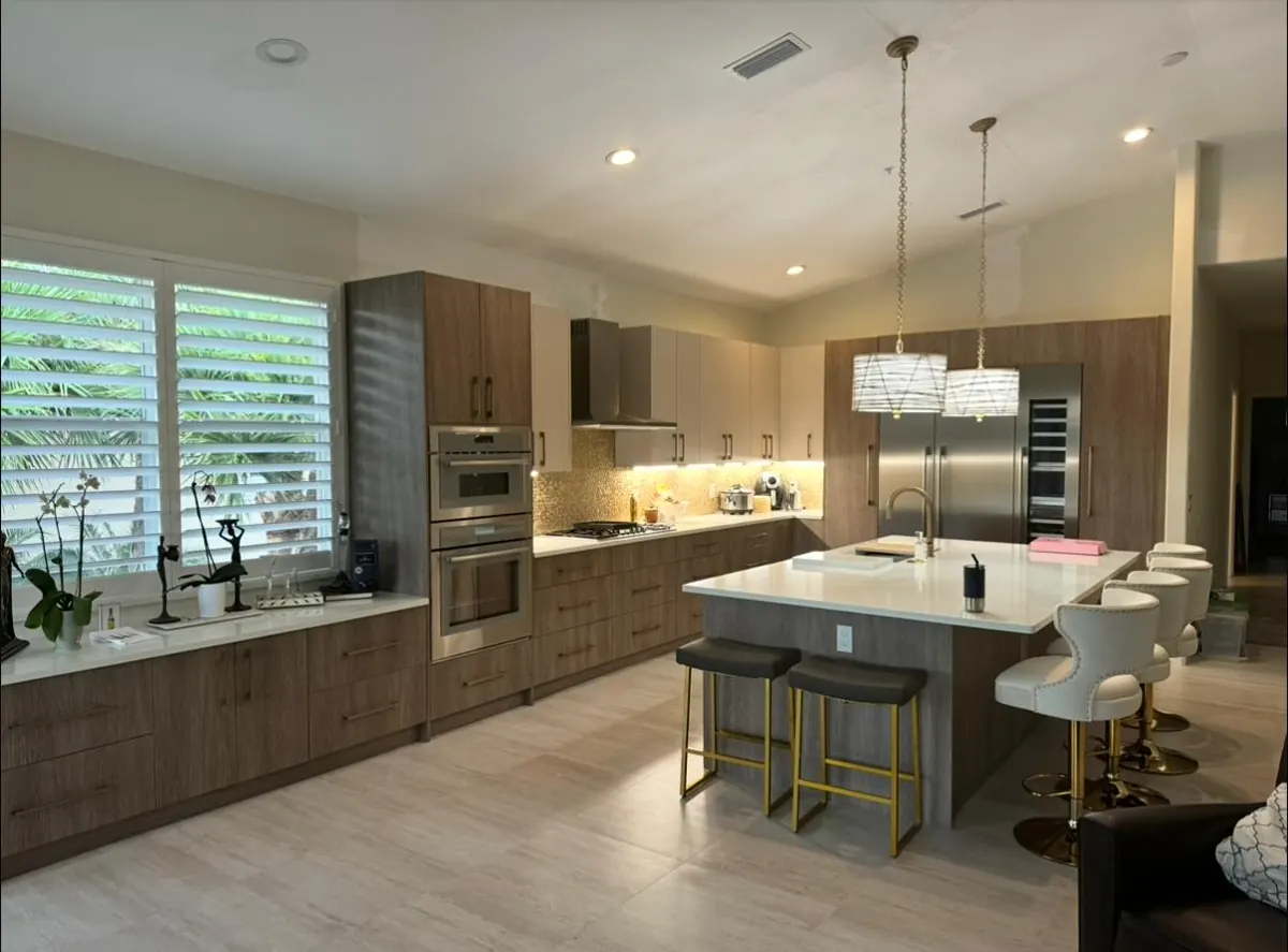 Wood-grain cabinets, double wall ovens, and an island with bar stools under crystal pendants
