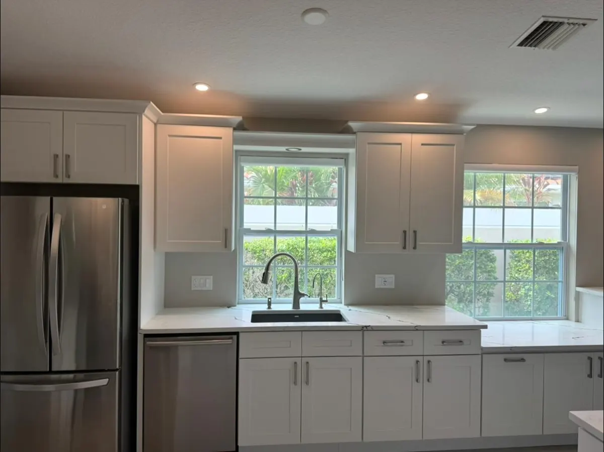White shaker cabinets around a window over the sink, with a stainless fridge