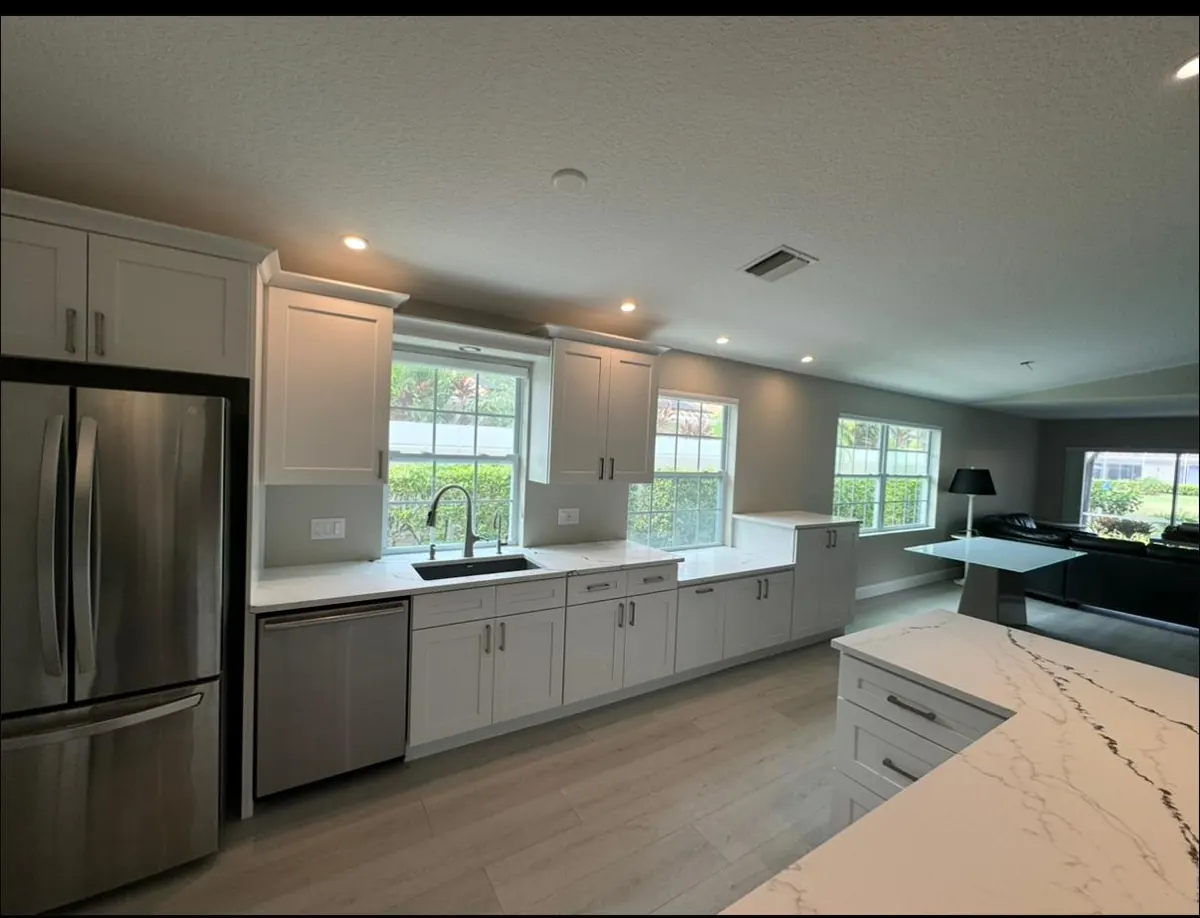 Open white kitchen with a stainless fridge and a marble-look island